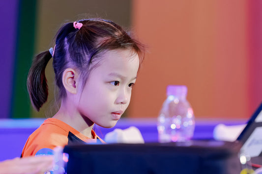Focused young girl at speedcubing competition table, colorful background, water bottle visible